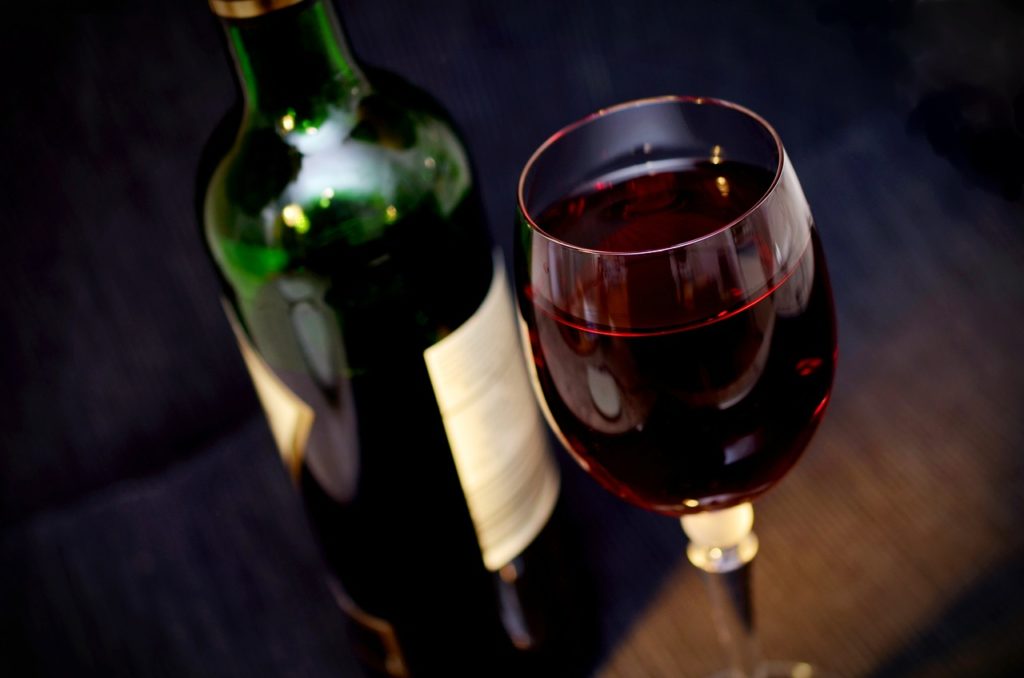 A moody image of a glass of red wine with the open bottle close to it.