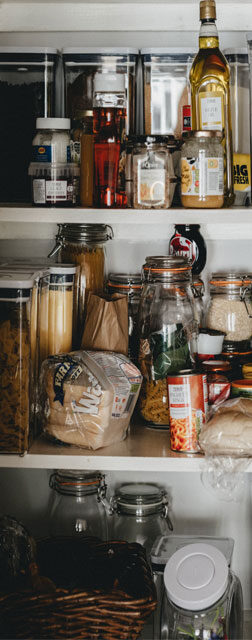 Selection of jars, tins, and bottles of food lining the shelves of a kitchen pantry.