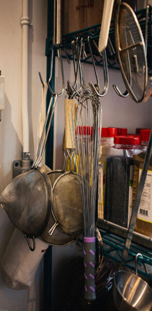 Collection of kitchen utensils hanging against a wall, waiting to be used.
