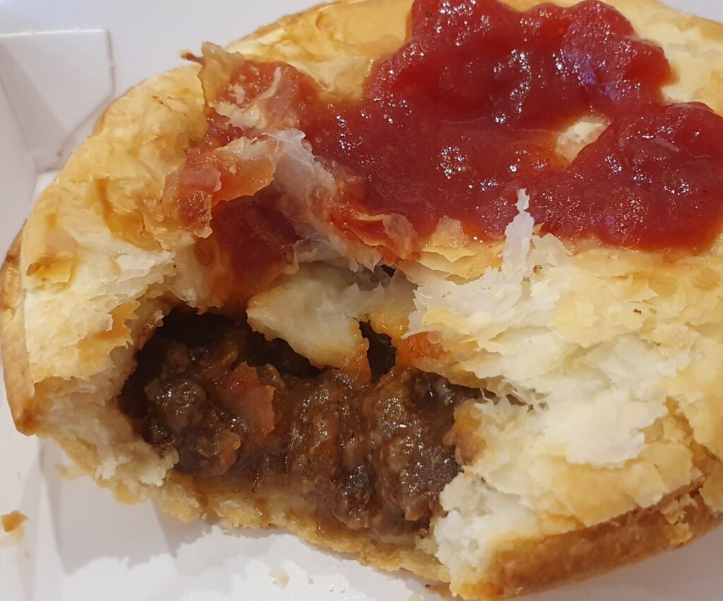 Aussie meat pie; served HOT, flaky pastry lid on a hot water pastry bottom, packed full of tender beef in a rich and thick gravy - always eaten with tomato sauce.