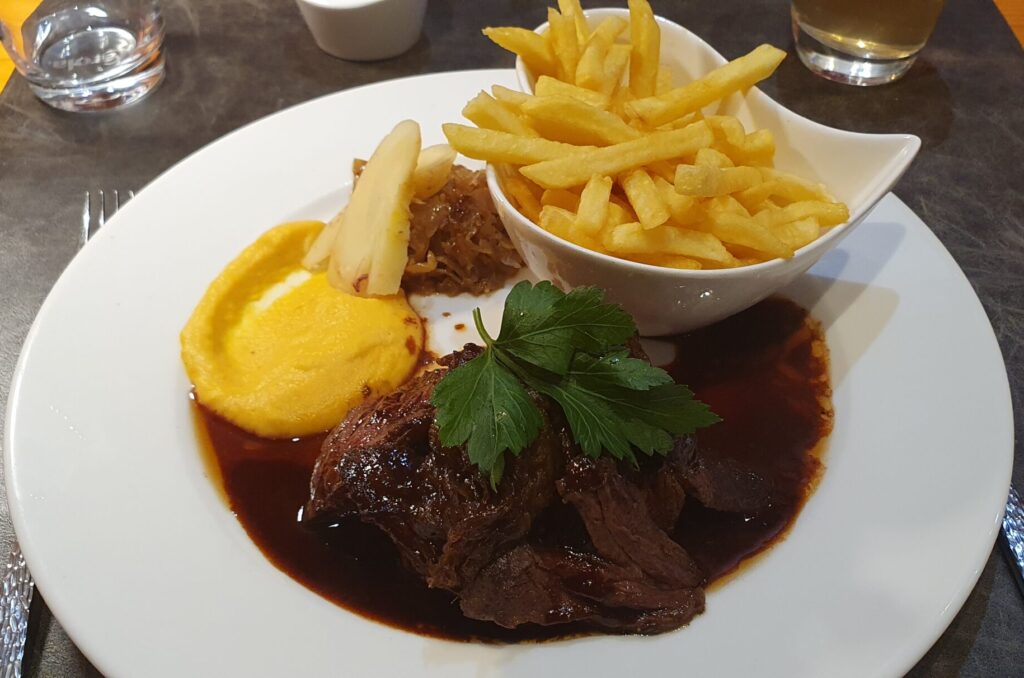 En Français; "Onglet de boeuf et sa fondue d'échalotes, sauce bordelaise, et pommes frites" In English: Beef flank steak with shallot fondue, Bordelaise sauce, and French fries A wide white plate with a medium-rare grilled flank steak, coated in a mountain of luxuriant caramelised shallots and sauce Bordelaise, a bowl of golden-fried chips sit in a bowl, crisp on the outside and fluffy on the inside. A hearty meal in cold and miserable weather.